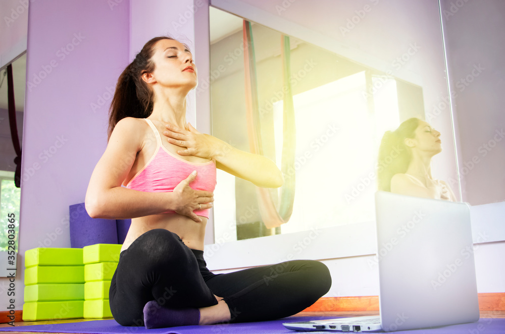 Fototapeta premium Fitness and yoga trainer teaches via laptop. Wireless technology in sports, self-isolation . The girl shows exercises in the gym on the mat. The concept of distance learning.