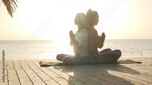 Two women practice closing meditation for partner yoga at seaside at sunset photo