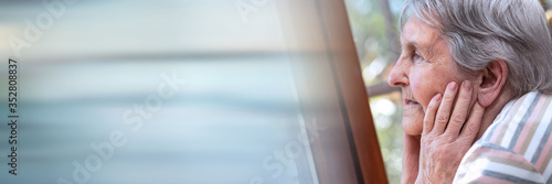 Elderly woman looking out the window; panoramic banner