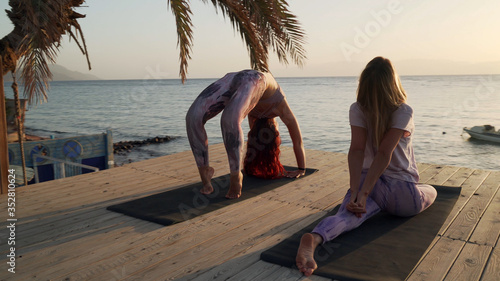 Two women practice yoga in seaside hotel lounge zone at sunset