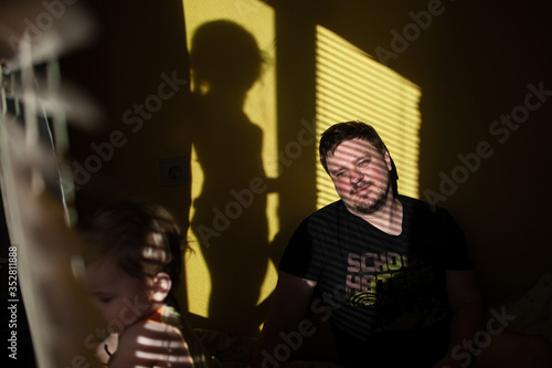  dad with children plays at home on a sunny day. family in the shade of the blinds. Dad and children having fun in the bedroom on a sunny day. The shadow of the blinds in the room with the family © sun_house_ann