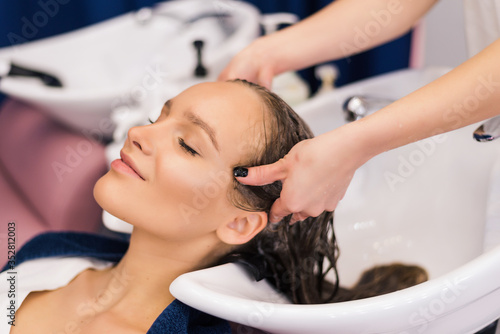 Hairdresser washing hair of happy young woman. Girl and do relaxing massage at beauty saloon