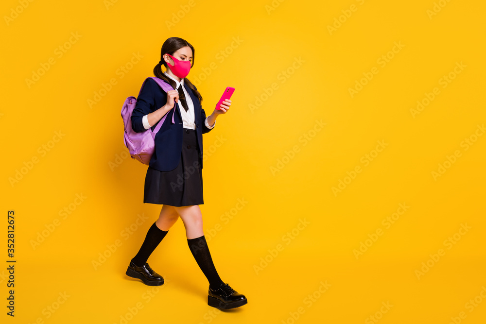 Full size profile side photo high school teenager go walk lesson use smartphone chatting wear black blazer jacket skirt long socks backpack medical mask isolated yellow color background Full size profile side photo high school teenager go walk lesson use smartphone chatting wear black blazer jacket skirt long socks backpack medical mask isolated yellow color background