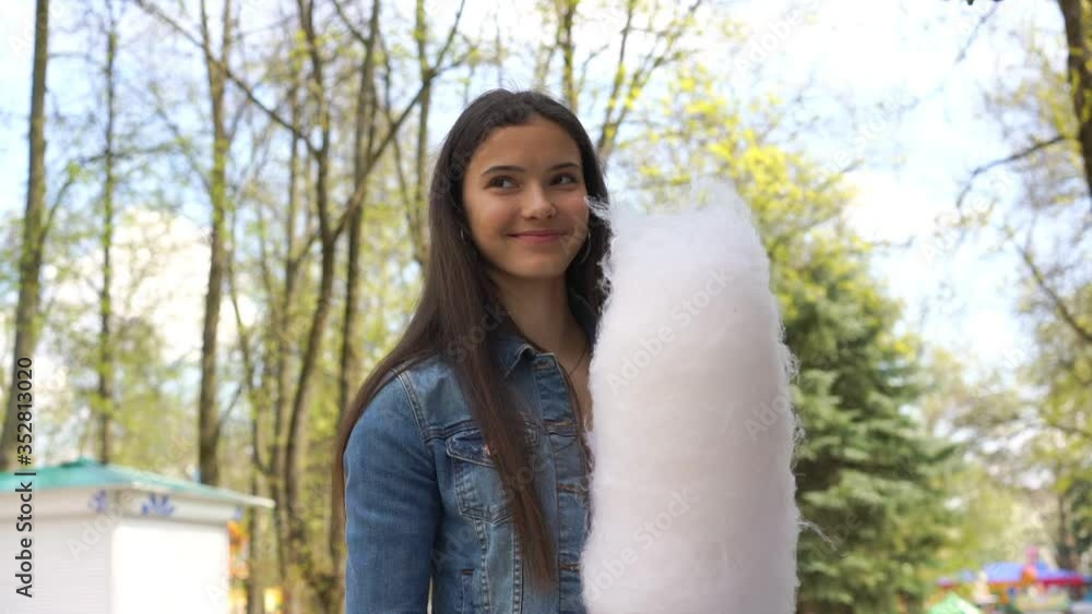 excited girl with long hair holds large cotton candy and walks along amusement park road slow motion close view excited girl with long hair holds large cotton candy and walks along amusement park road slow motion close view