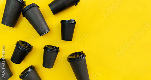 Many black take away coffee cups lay on yellow background, banner fomat, copy space, closeup, flatlay. photo