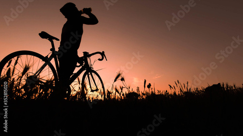 Silhouette of cyclist man drinking water during a sunset in nature