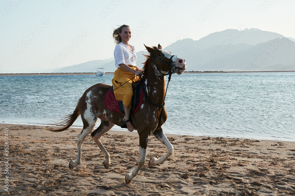 Caucasian blonde girl riding horse at sunset beach Caucasian blonde girl riding horse at sunset beach