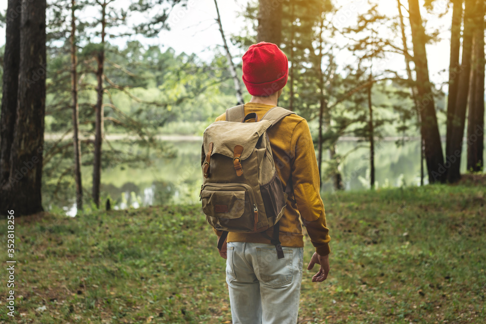 Tourist with a backpack and a red hat is walking in the forest among the trees. Active trekking and unity with nature