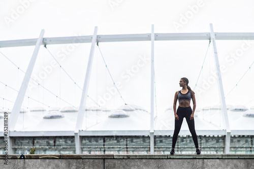 Keep your body in good shape. Slender young woman in sportswear stands in confident pose, a stadium on background