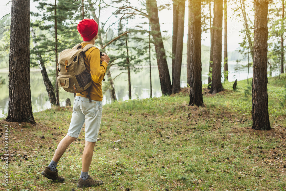 Tourist with a backpack and a red hat is walking in the forest among the trees. Active trekking and unity with nature Tourist with a backpack and a red hat is walking in the forest among the trees. Active trekking and unity with nature
