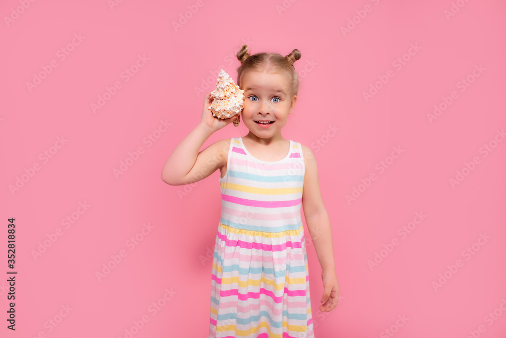 Portrait of blonde surprised child girl listen a seashell at the pink studio background. Summer vacation, ear diseases, otitis concept