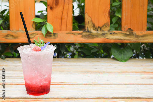 Strawberry Italian soda with butterfly pea flowers in plastic glass on wooden table.
