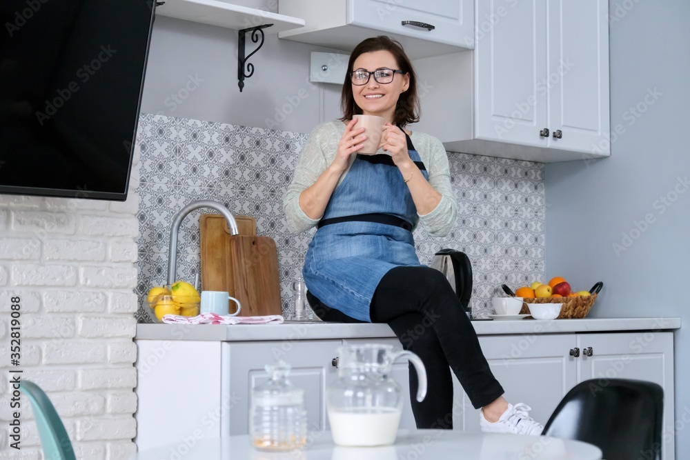 Portrait of housewife woman in apron at home in kitchen with cup of drink Portrait of housewife woman in apron at home in kitchen with cup of drink