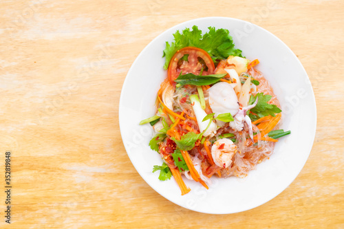 spicy vermicelli salad with seafood in white dish on wooden table.