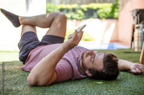 Young man lying on the grass in a garden using the phone. Man on the phone