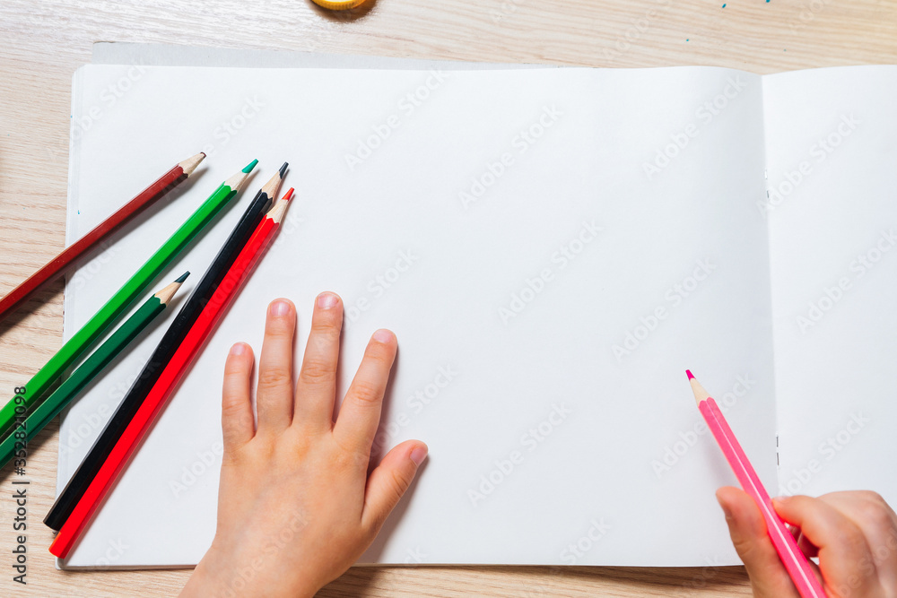 A small child draws in the album on the table. Around colored pencils and paints. Сору space A small child draws in the album on the table. Around colored pencils and paints. Сору space
