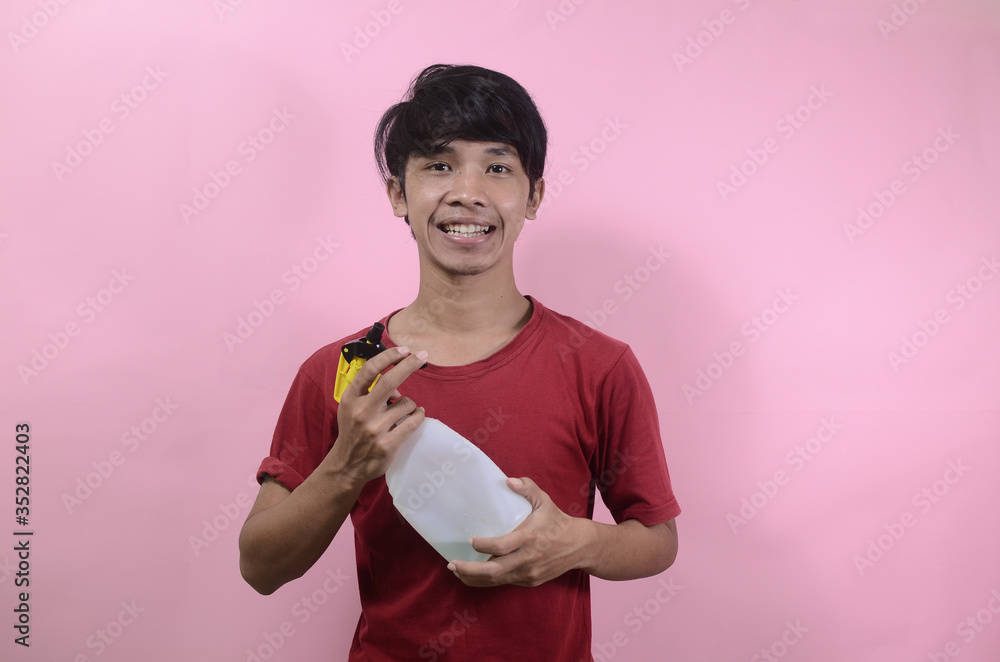 Man with water sprayer in hand. Asian men wearing red t shirts isolated on a pink background Man with water sprayer in hand. Asian men wearing red t shirts isolated on a pink background