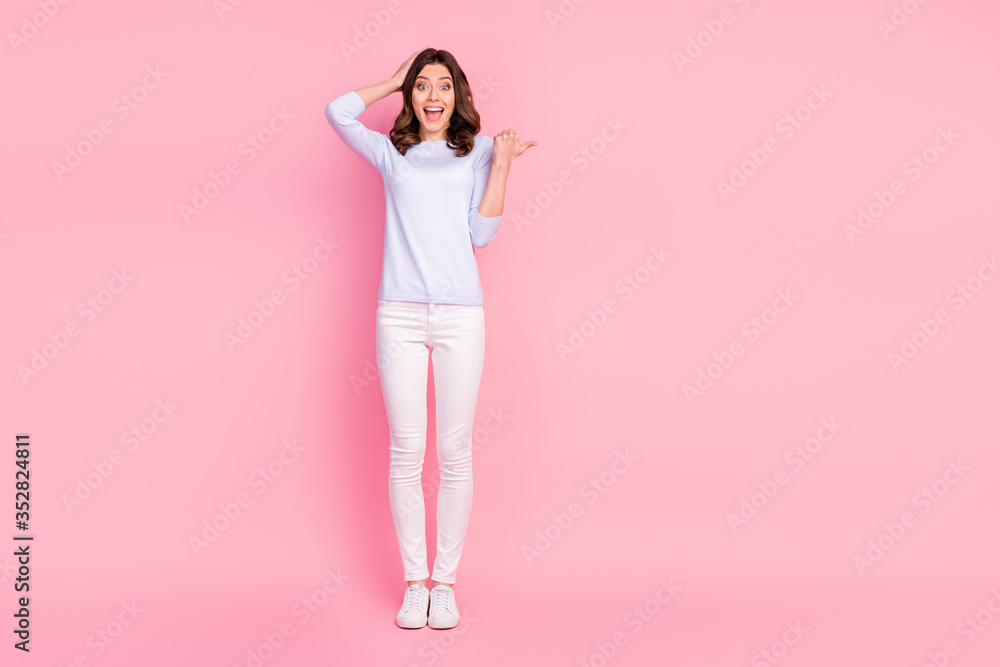 Full size photo of attractive shocked lady good mood directing finger empty space showing novelty product wear casual white pullover trousers sneakers isolated pink color background Full size photo of attractive shocked lady good mood directing finger empty space showing novelty product wear casual white pullover trousers sneakers isolated pink color background