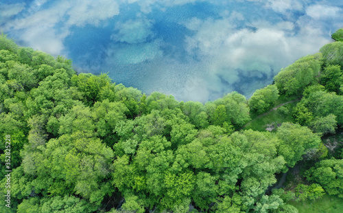 Aerial view of a shoreline with trees and a river with a reflection of the sky