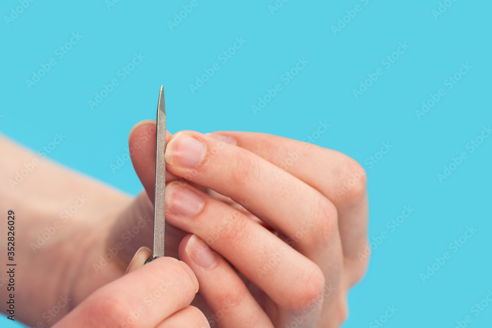 Woman polishes nails with a nail file on a blue background, close-up, copy space. The idea of self-care of nails, hands Woman polishes nails with a nail file on a blue background, close-up, copy space. The idea of self-care of nails, hands