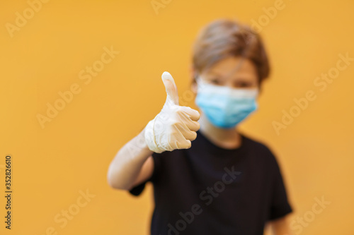 School boy wearing medical mask and gloves to protect from virus, showing thumbs up photo