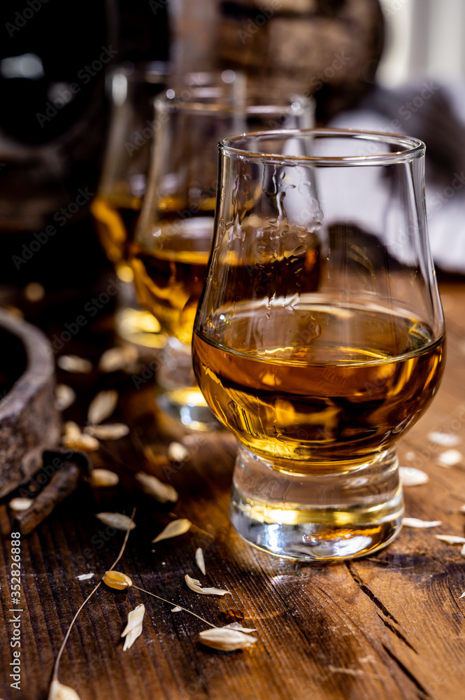 Small tasting glasses with aged Scotch whisky on old dark wooden vintage table with barley grains Small tasting glasses with aged Scotch whisky on old dark wooden vintage table with barley grains