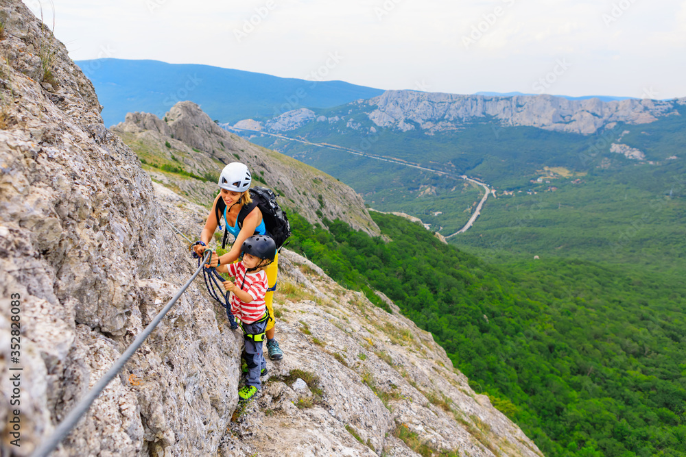 Young mother, child in safety equipment climb to mount top by via ferrata beginner route. Family travel adventure, hiking activity. Kids exploring nature on summer vacation. Weekend day walking tour