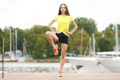Young woman in sportswear is warming up and stretching on promenade