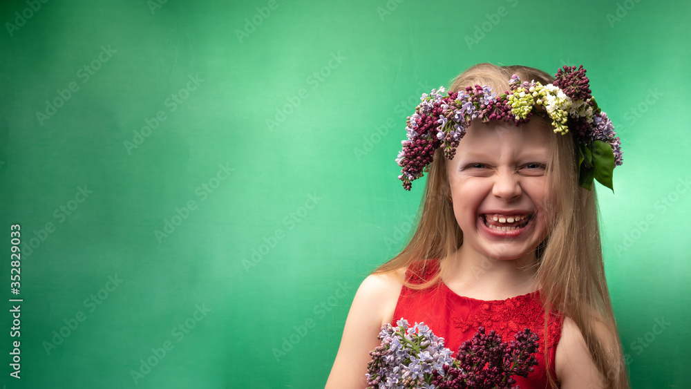 Fototapeta premium Charismatic young beautiful in a lilac wreath is having fun on a green background, with daylight. Flaunts grimace
