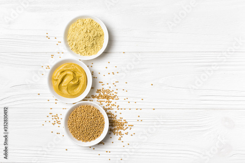 Canvas Print Set of yellow mustard sauce, powder and seeds in small white bowls