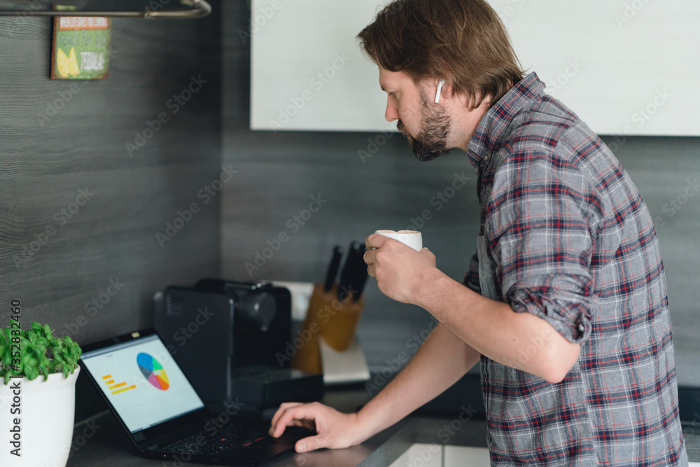 mann arbeitet im Homeoffice in der Küche am tablet, trinkt einen Kaffee und telefoniert mit bluetooth-kopfhörern mann arbeitet im Homeoffice in der Küche am tablet, trinkt einen Kaffee und telefoniert mit bluetooth-kopfhörern
