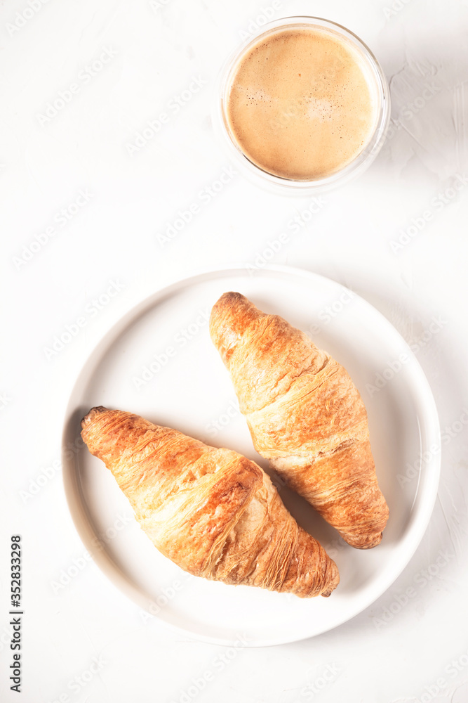 Two croissants on a plate next to a cup of coffee on light gray background. Top view layout. Two croissants on a plate next to a cup of coffee on light gray background. Top view layout.