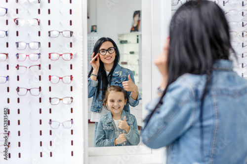 Beautiful little girl in optics store together with mom choose new glasses