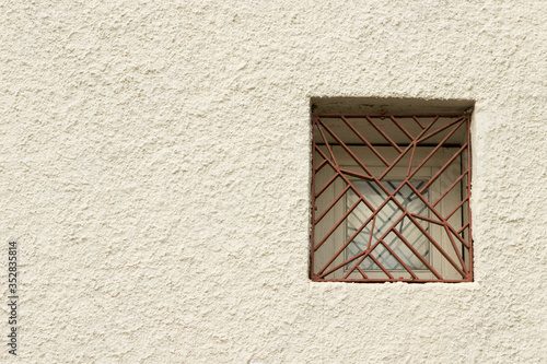 Small window with glass and brown metal bars on a light beige stucco wall