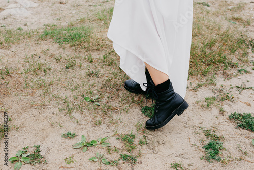 Women's feet in rough black boots. It stands on the beach on the sand. Runaway bride.