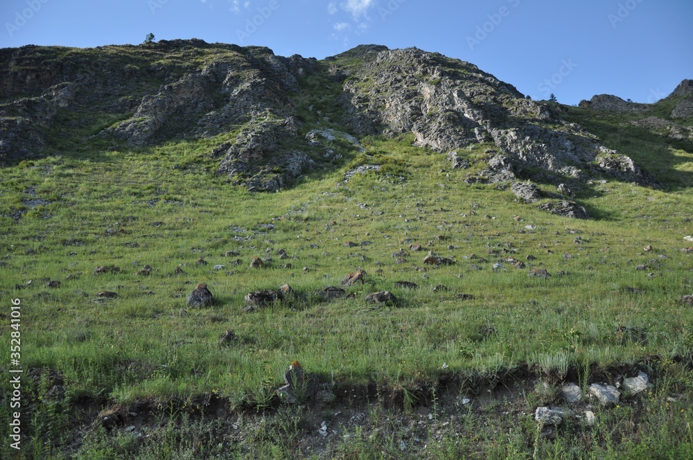 The slope of the mountain, covered with grass, stones and rock fragments against the blue sky
