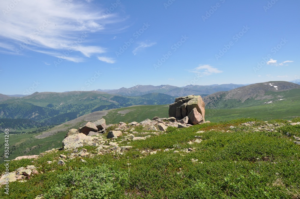 A piece of rock and stone fragments on top of a mountain covered with grass against the background of other mountains and sky