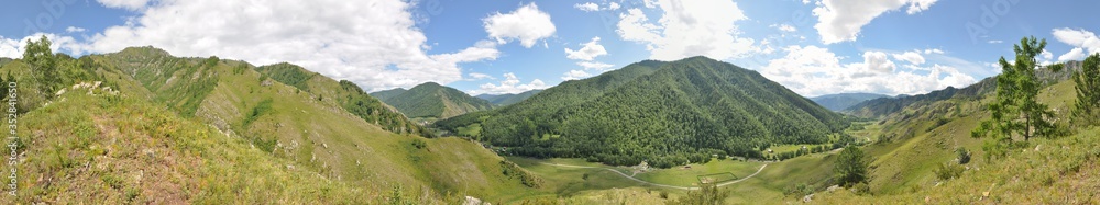 Panorama of mountains covered with forest and grass, with a road and a village below