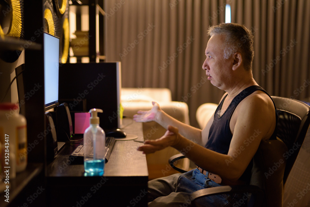Mature Japanese man using computer and shrugging shoulders at home