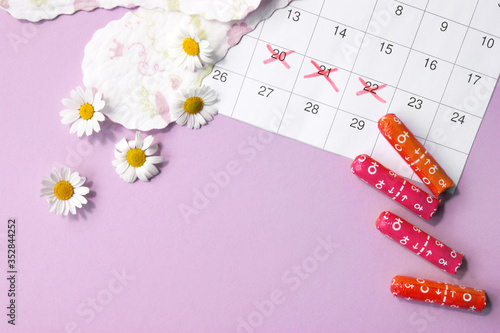 Menstrual pads and tampons on menstruation period calendar with chamomiles on pink background.