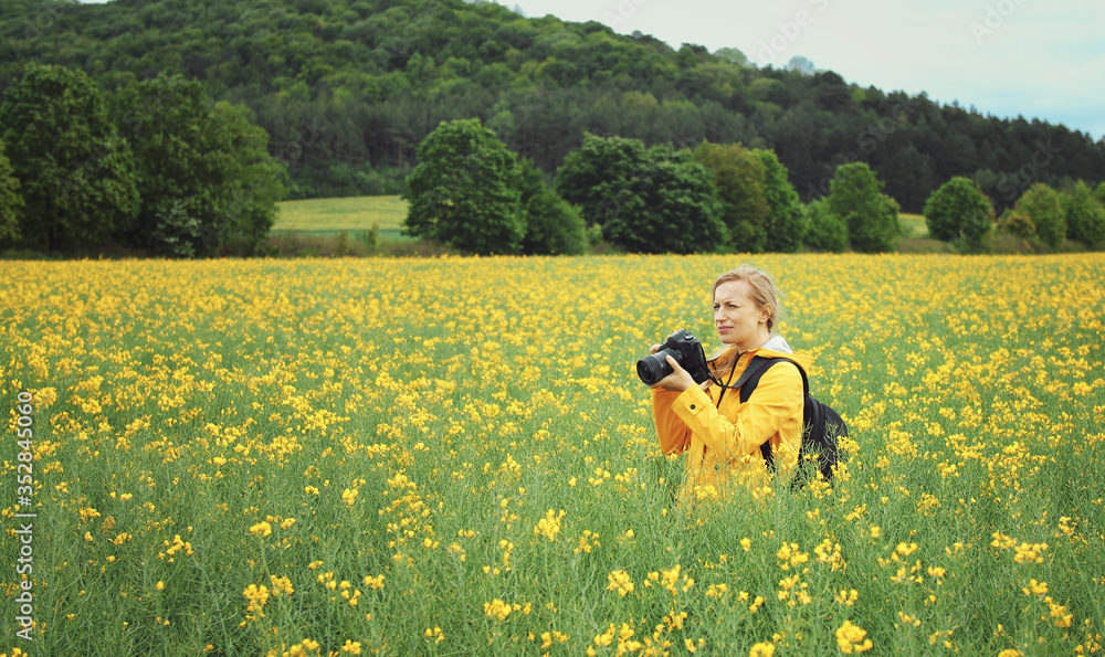 Female photographer standing among blossoming rapeseed looking for better landmark