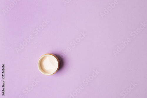 opened jar with cream on purple background. top view with copy space