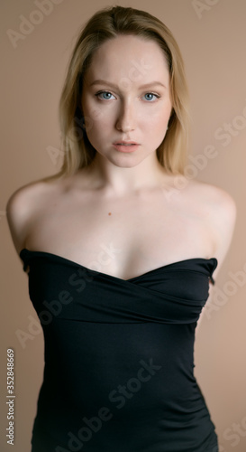 Graceful young woman in a black top posing against beige wall. © Vladimir Arndt