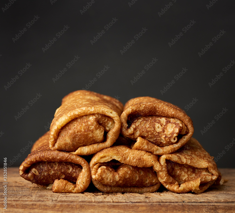 twisted thin fried pancakes with filling lie in a stack on a wooden board