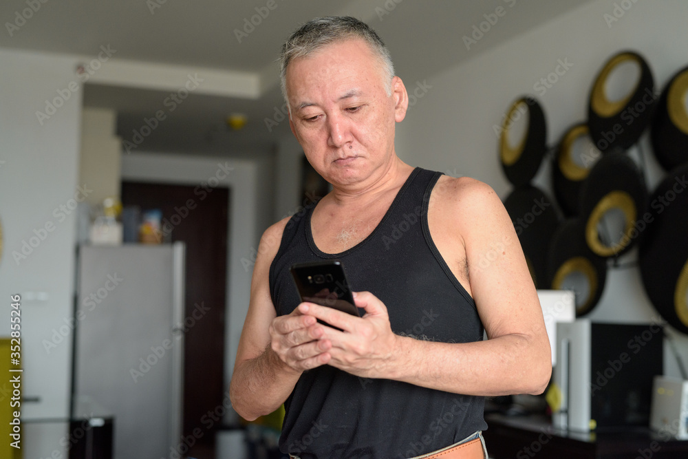 Portrait of mature Japanese man using phone at home Portrait of mature Japanese man using phone at home
