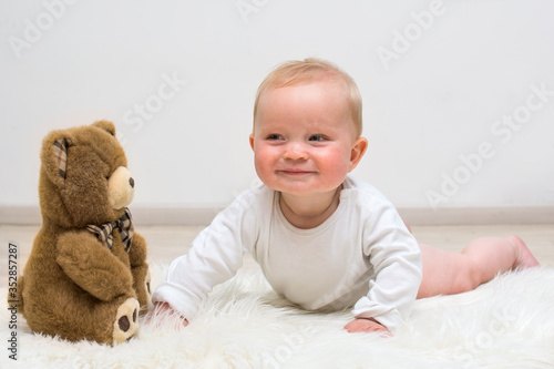 Little baby boy and teddy bear lying on the floor and smiling