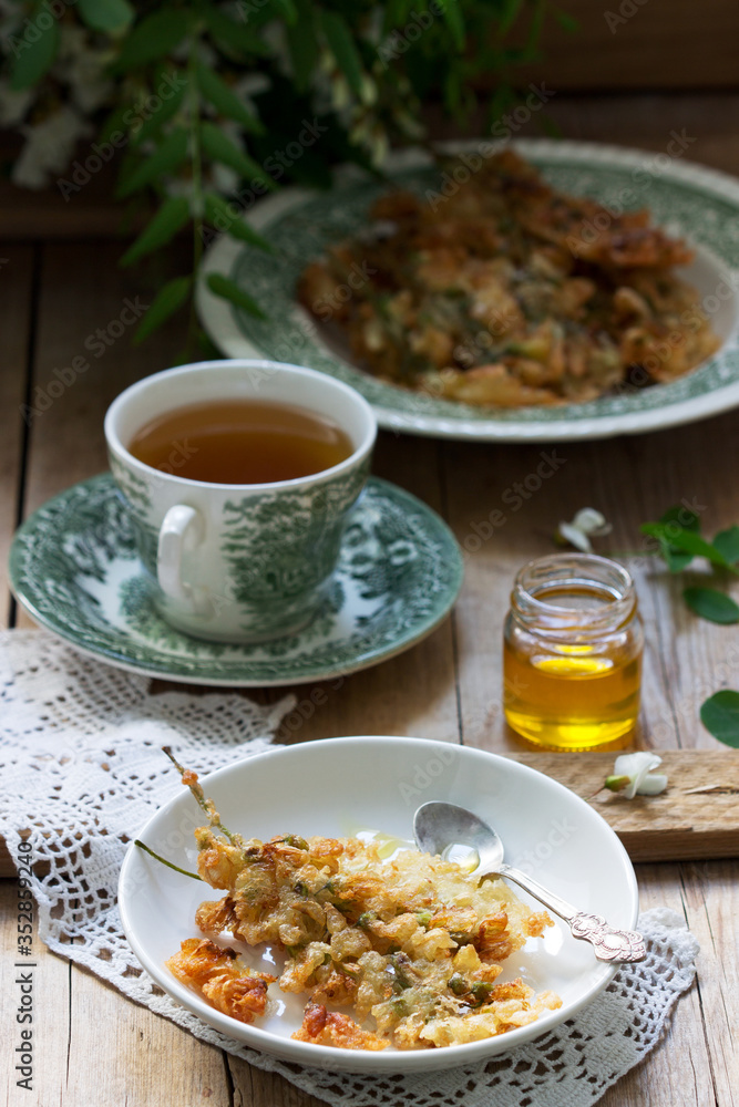 Robinia fritters served with tea and honey on a wooden table. Rustic style.