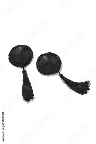 Detailed shot of two black fabric nipple covers decorated with lace ribbons and black silk tassels. The pair of pasties is isolated on the white background.  photo