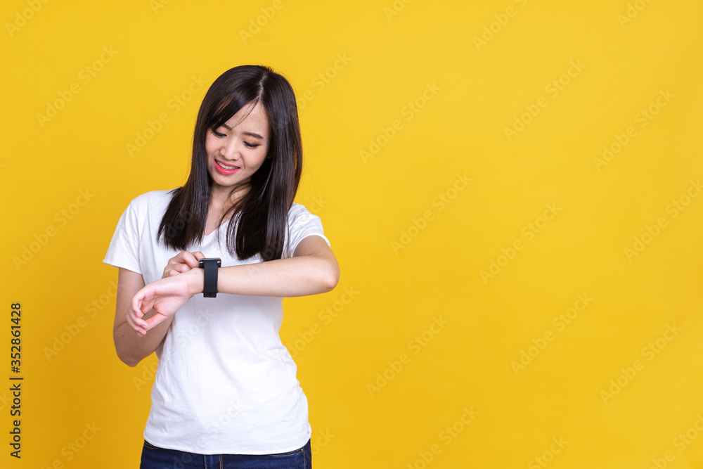 Portrait of young Asian woman holding hand with wrist watch and looking or pointing to watch isolated on yellow background Portrait of young Asian woman holding hand with wrist watch and looking or pointing to watch isolated on yellow background