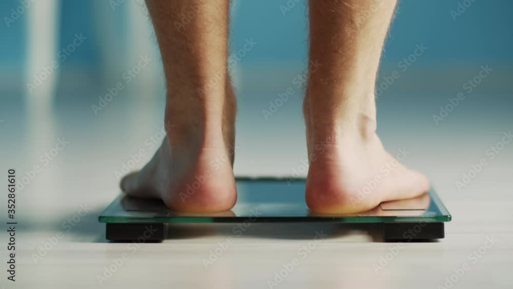 Bare male legs, steps on the scales, is weighed and walks away, healthy eating, weight loss Bare male legs, steps on the scales, is weighed and walks away, healthy eating, weight loss